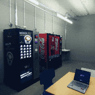 (a desk with a laptop in a concrete room with two vending machines and sterile lighting)