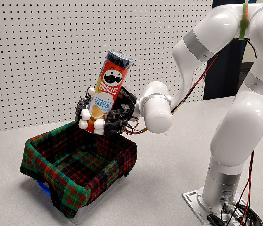  A white robot arm grasps a can of Pringles lightly salted potato chips.