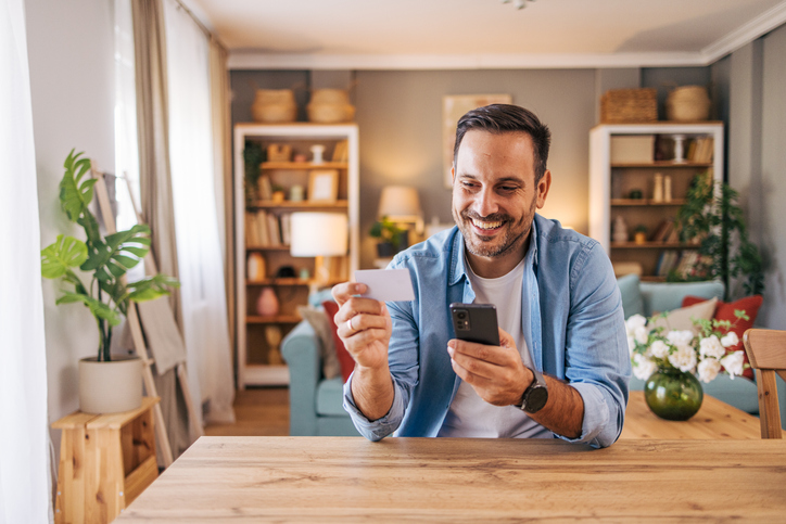 egy férfi bankkártyával és telefonnal a kezében otthon