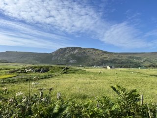 Green grass and rugged hill under a blue sky with wisps of cloud.