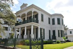 a large white house with green shutters and balconies on the second story