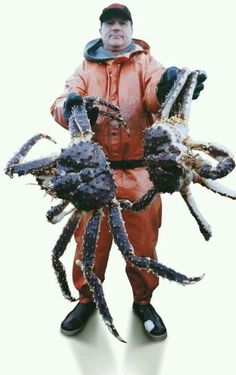 a man in an orange suit holding two large crabs