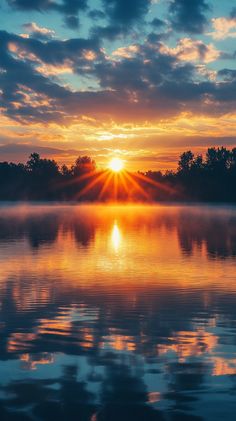 the sun is setting over some water with trees in the background and clouds in the sky