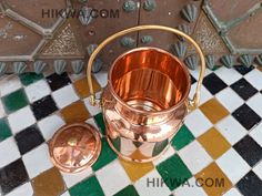 an old fashioned copper bucket and lid on a checkered tile floor