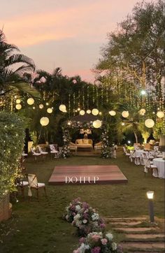 an outdoor wedding setup at dusk with lights strung from the ceiling and flowers on the ground