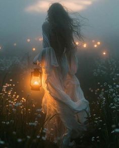 a woman holding a lantern in her hand while walking through a field with flowers at night