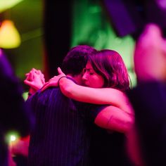 two people hugging each other in front of a crowd at a dance party with colored lights