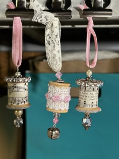 three bells are hanging from a rack with pink ribbon and beads on it's sides