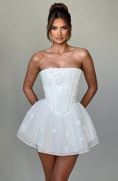 a woman in a short white dress posing for the camera with her hands on her hips