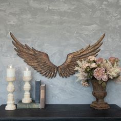 a vase filled with flowers next to an angel wings wall decoration on top of a mantle