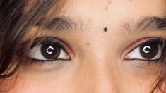 a close up of a woman's eyes with black dots on her forehead and eyebrows