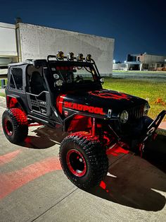 a red and black jeep parked next to a building