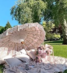 an open umbrella sitting on top of a lush green field next to pillows and flowers
