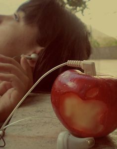 a woman laying on the ground next to an apple with ear buds in her mouth