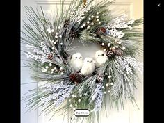 two little white birds sitting on top of a pine cone wreath with berries and cones