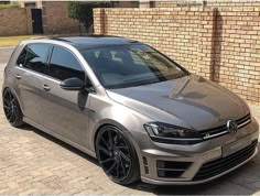 a silver volkswagen golf gtr parked in front of a brick wall with black rims