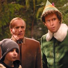 two men and a boy are standing in front of some trees wearing elf hats on their heads