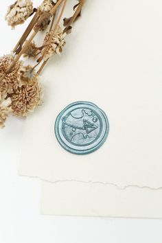 a piece of paper with a sticker on it and dried flowers in the background