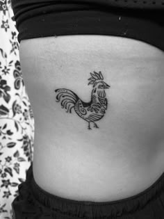 a woman's stomach with a small rooster tattoo on her lower side ribcage