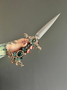 a person holding a knife in their hand with some jewelry on it's handle