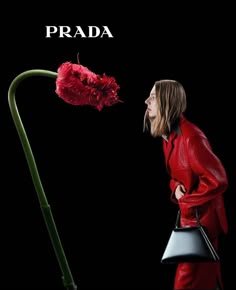 a woman in a red coat is looking at a flower with the words prada on it