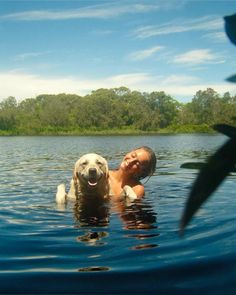 a woman and her dog are swimming in the water with trees in the back ground