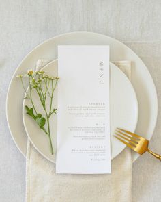 a place setting with flowers and a menu on a white plate next to a gold fork