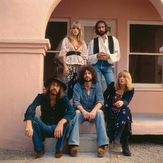 a group of people sitting on top of a bench in front of a pink building