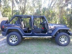 a blue jeep parked in the grass near some trees and bushes with its doors open
