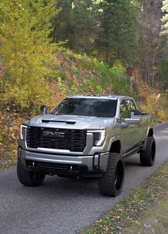 a silver truck driving down a road next to trees and bushes on both sides of the road