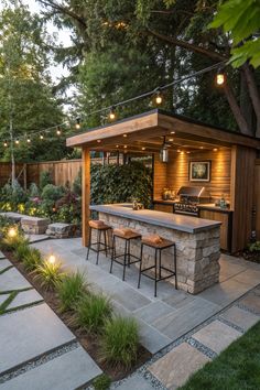 an outdoor kitchen and bar area with lights on the roof, surrounded by greenery