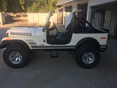 a white jeep is parked in front of a garage with its door open and the driver's seat up
