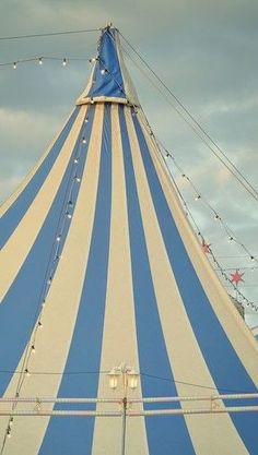 a large blue and white striped tent with string lights on the top, in front of a cloudy sky