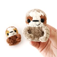 two small stuffed animals sitting next to each other on a white surface in front of a hand