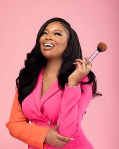 a woman in a pink suit holding a makeup brush and looking up at the camera