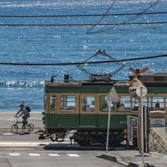 a green and yellow train traveling down tracks next to the ocean on a sunny day