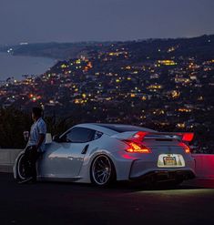 a man sitting on the back of a sports car in front of a city at night