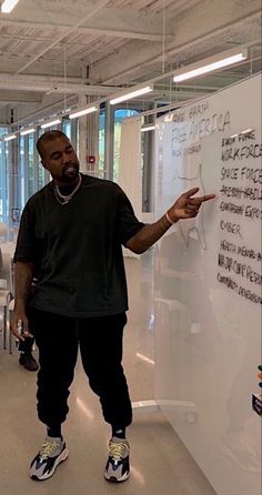 a man standing in front of a whiteboard with writing on it and pointing to the side
