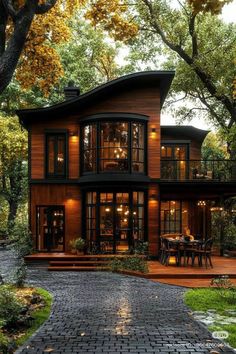 a large wooden house with lots of windows and lights on the front porch, surrounded by trees