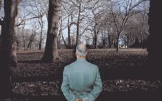 an old man standing in the woods with his back to the camera, looking at trees