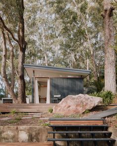 there is a small house in the woods with trees around it and a large rock on the ground