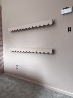 two white shelves on the wall in a room with pink walls and carpeted floor