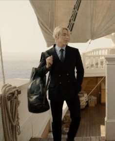 a man in a suit is standing on the deck of a boat with a bag