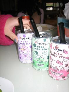 three hello kitty cans are sitting on a table with one holding a cell phone and the other has a straw in it
