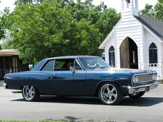 an old blue car parked in front of a white church with a steeple on top
