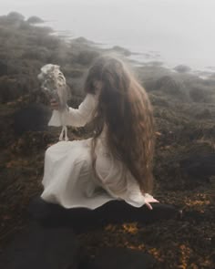 a woman with long hair sitting on the ground holding an owl in her hand and looking at it