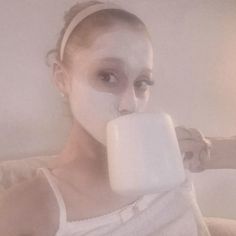 a woman with white makeup drinking from a mug