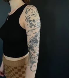 a woman with a tattoo on her arm and sleeve is standing in front of a black wall