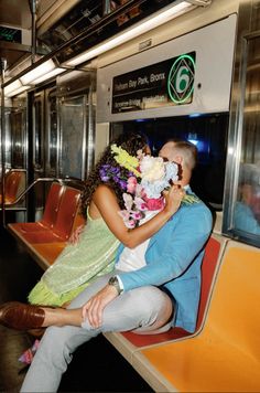 a man and woman sitting on a train with flowers in their lap as they kiss