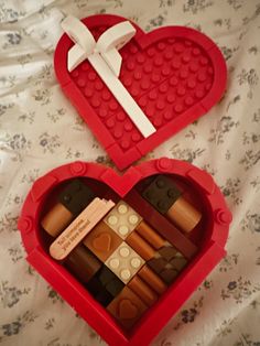 two heart shaped boxes filled with legos on top of a bed next to each other